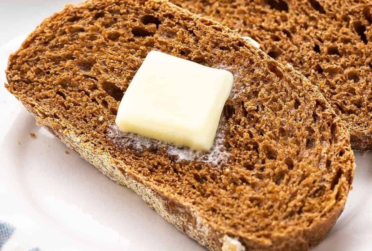 Two slices of brown bread, one with a pat of butter on it.