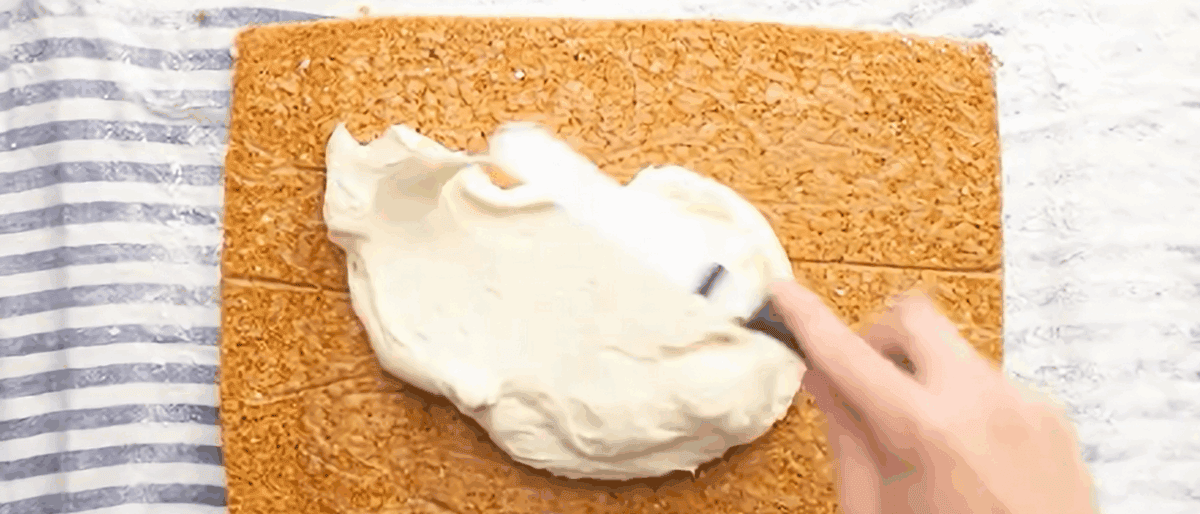 Spreading cream cheese over the unrolled cake. 