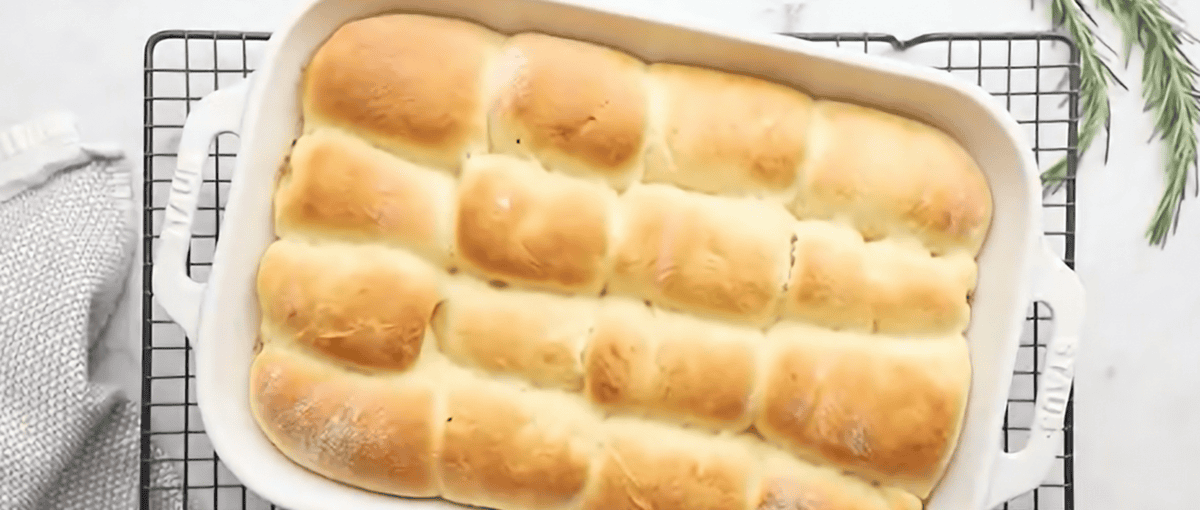 Parker House Rolls are soft, buttery, and slightly sweet with a honey and rosemary butter inside and glaze on the outside. A baking dish of Parker House rolls on a cooling rack.