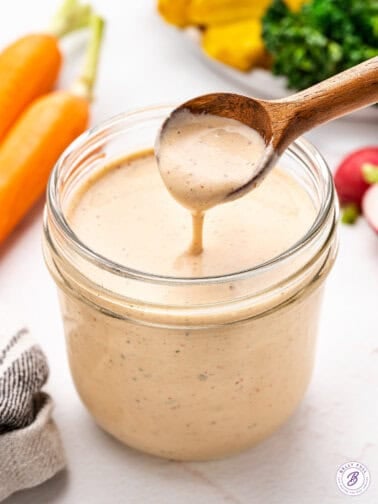 A wooden spoon over a jar of salsa ranch salad dressing