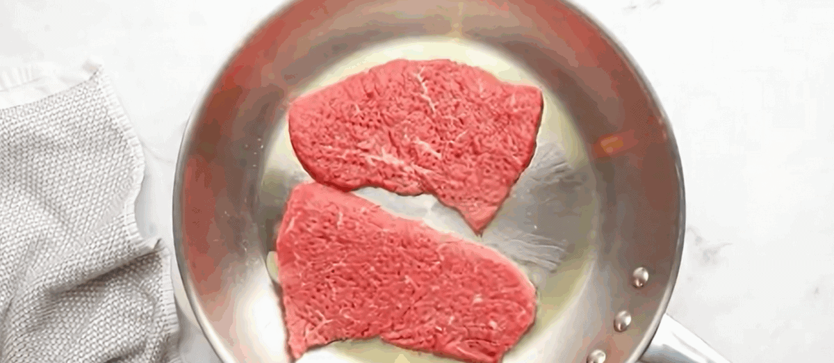 Searing the steak in a stainless steel pan.