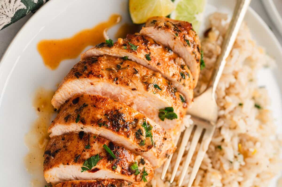 Slices of garlic lime chicken on a plate with rice and a fork.
