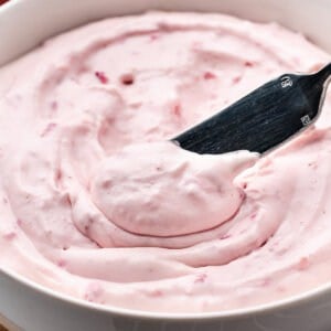 A knife diving into a bowl of strawberry cream cheese