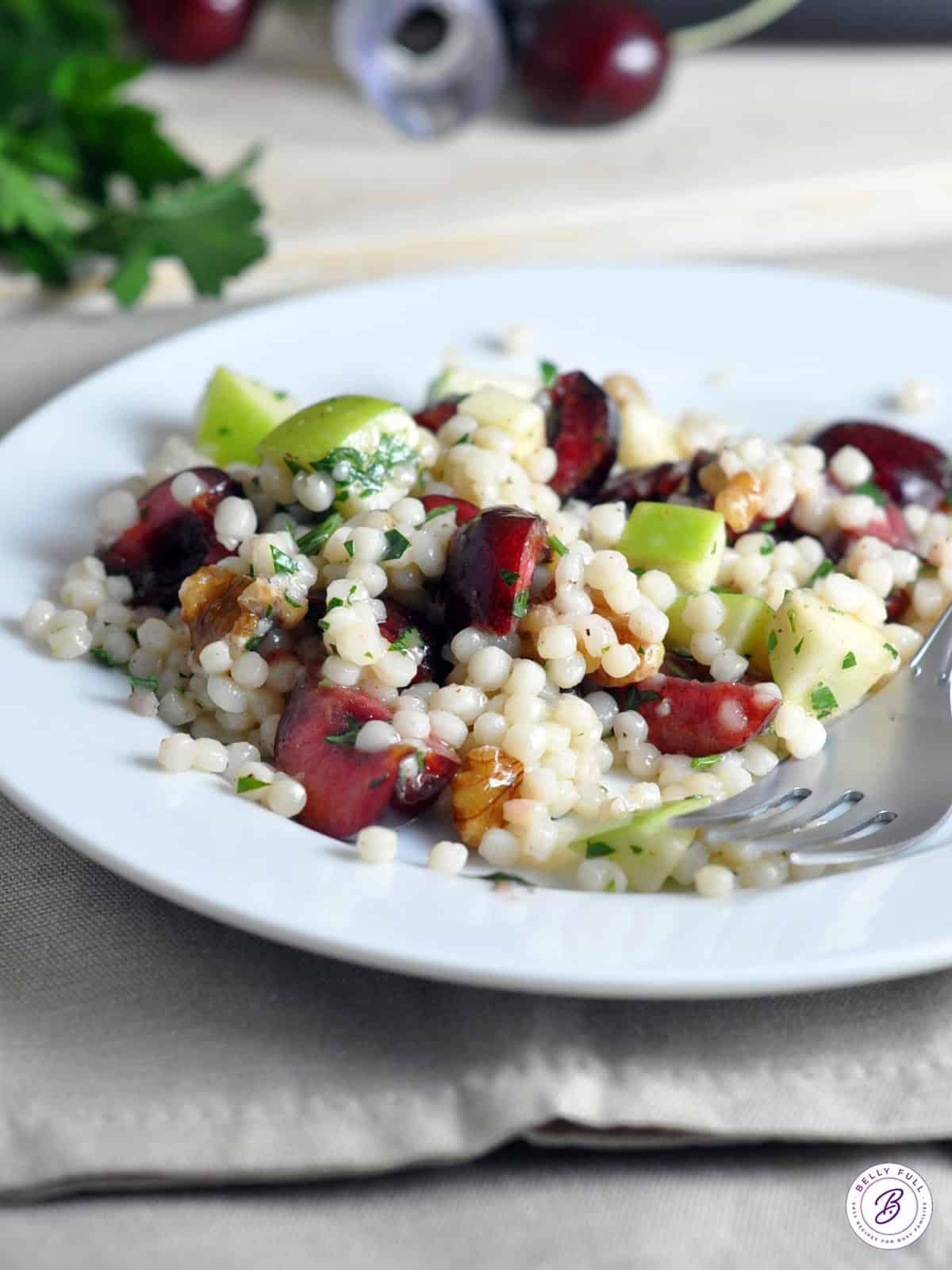 portion of Israeli Couscous Salad with cherries and apples on white plate