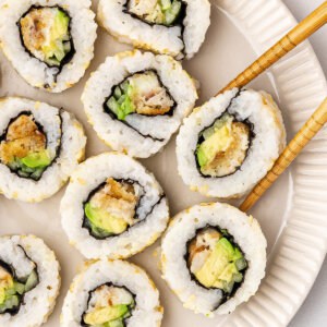 Chopsticks grabbing a piece of a fish finger sushi roll from a plate