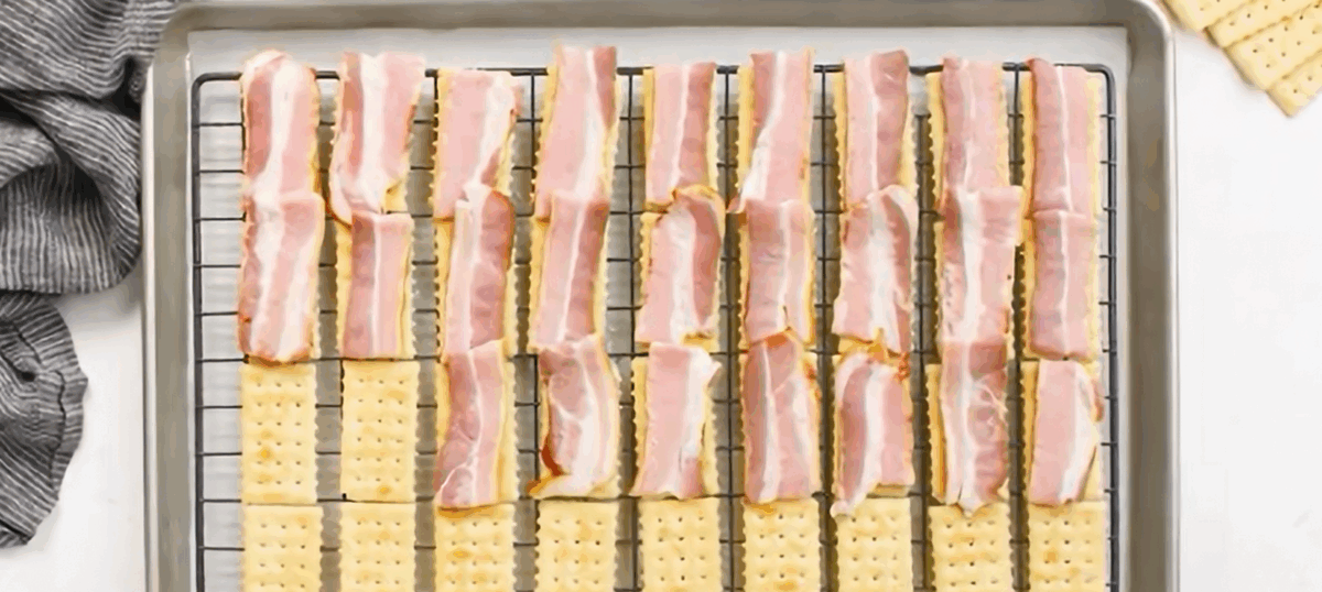 Placing a piece of bacon on top of each cracker.