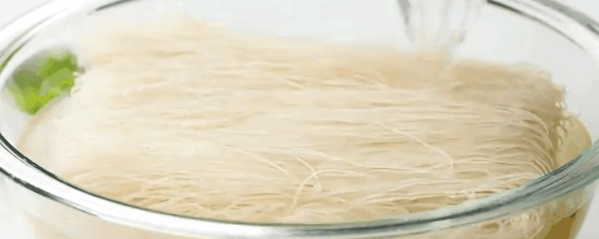 Water being poured over rice noodles in a glass bowl.