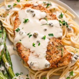 A plate of chicken with caper cream sauce over pasta