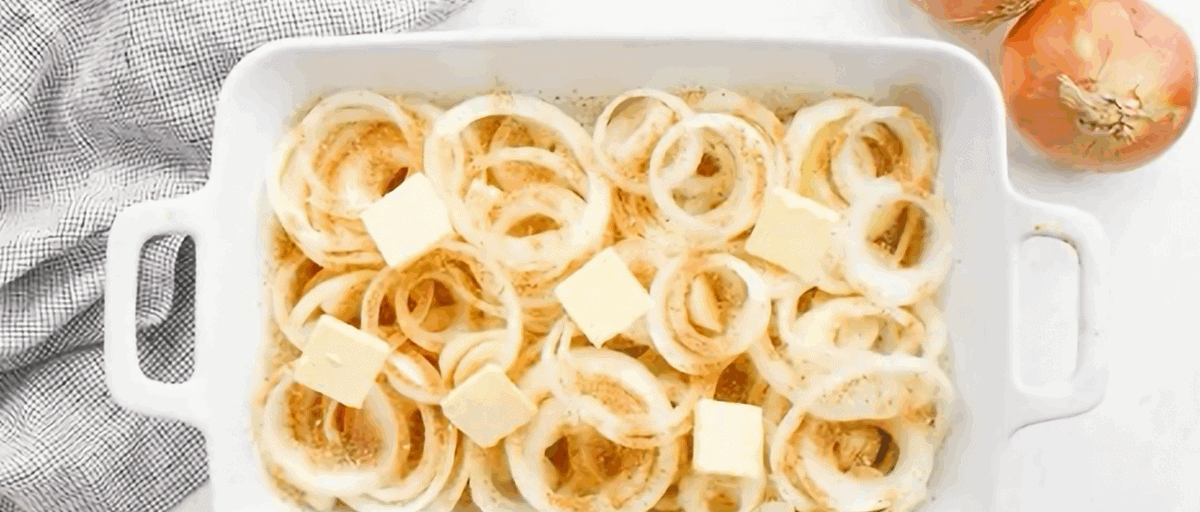 Pats of butter on top of the onions in a white casserole dish.