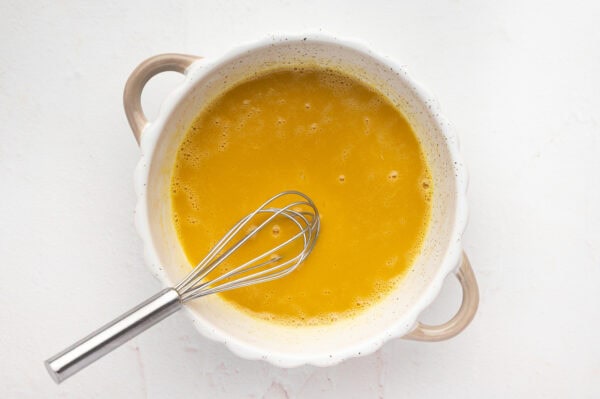 Eggs and vanilla mixed together in a pot with a whisk.