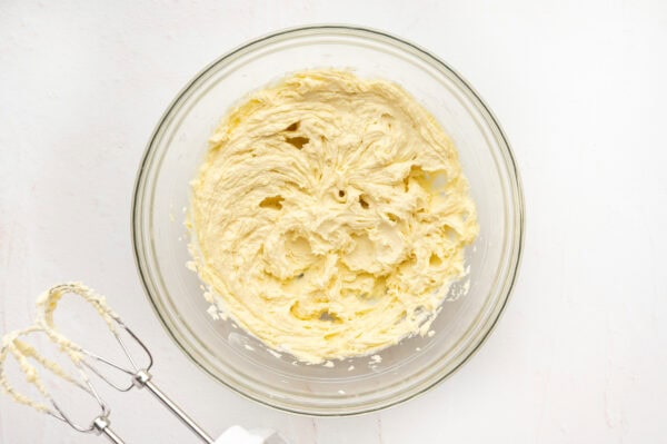 Butter, sugar, eggs, and vanilla mixed together in a glass mixing bowl.