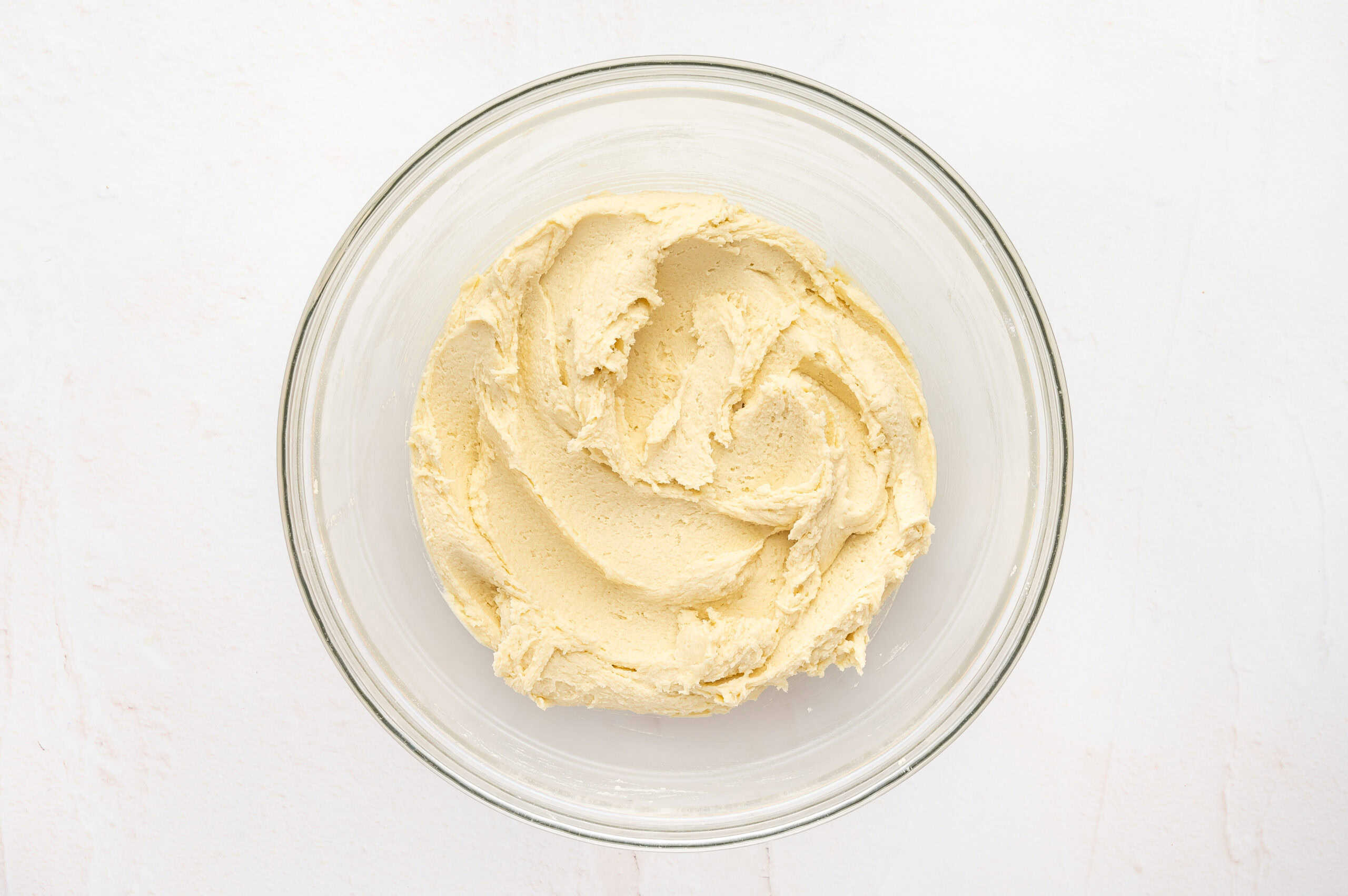 Butter cookie dough with flour added in a glass mixing bowl.