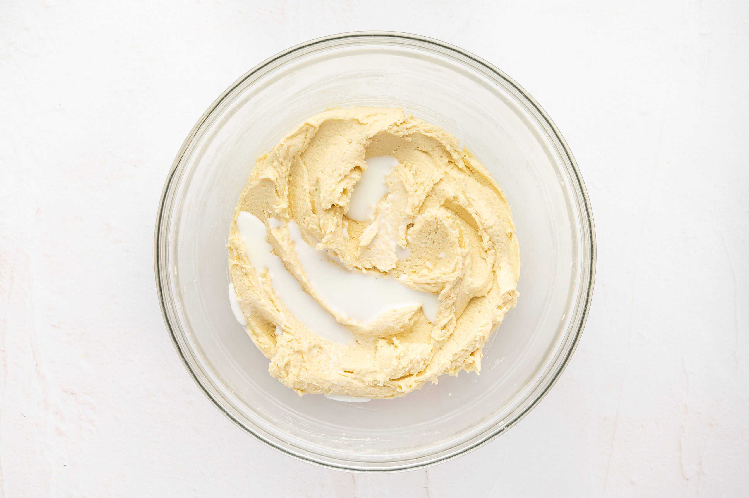 Milk added to wet ingredients for butter cookies in a glass mixing bowl