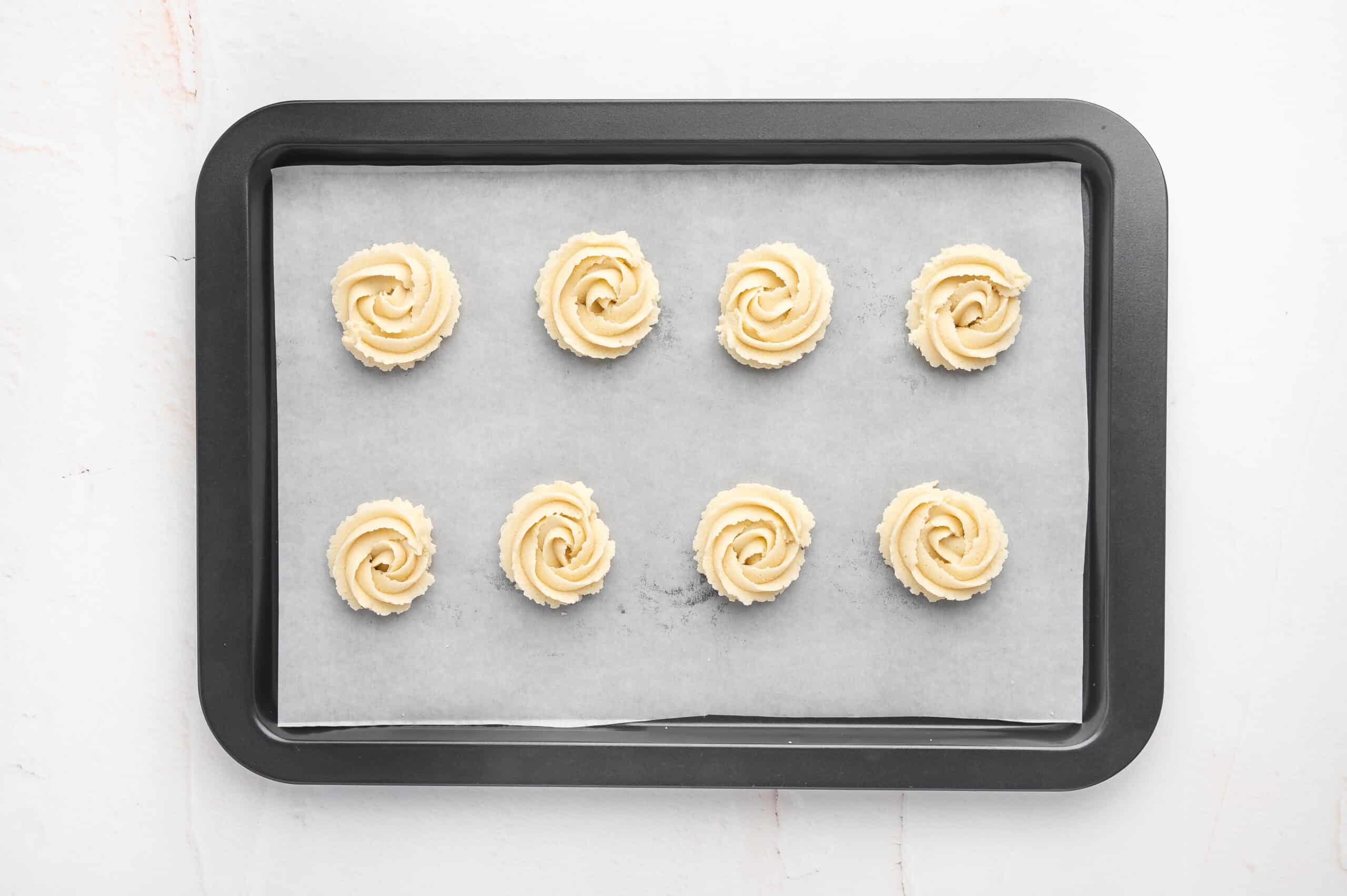 Swirls of butter cookie dough on a parchment lined baking sheet.