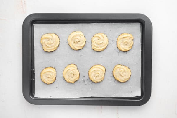 Freshly baked butter cookies on a parchment lined baking sheet.