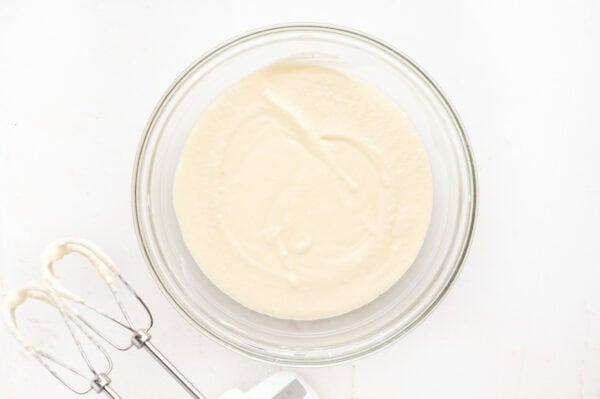 Cream cheese, heavy cream, powdered sugar, and butter combined in a glass mixing bowl.