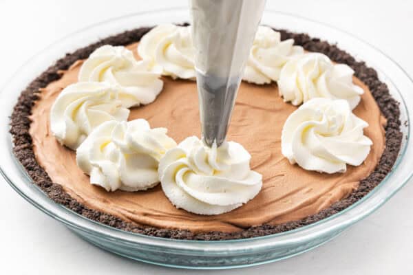 A piping bag piping swirls of whipped cream on a french silk pie.