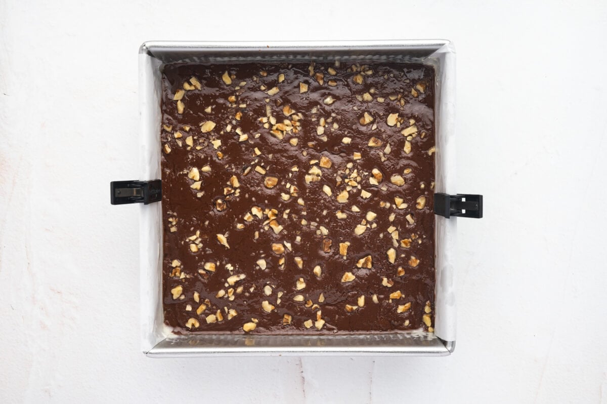 Fudge mixture in a parchment lined baking dish topped with walnuts.