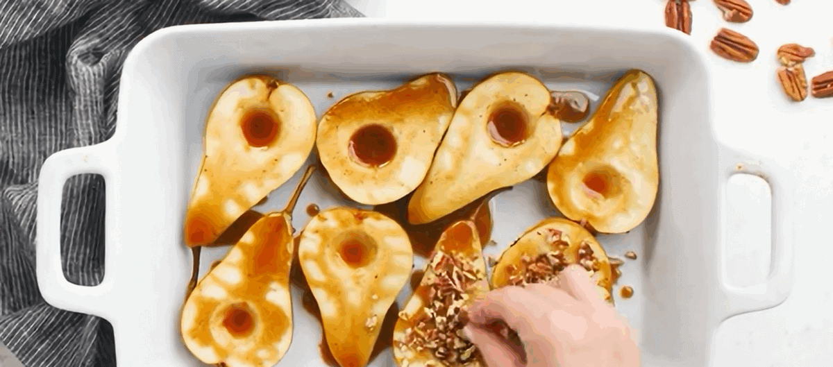 Pears drizzled with honey mixture and topped with pecans in a white casserole dish.