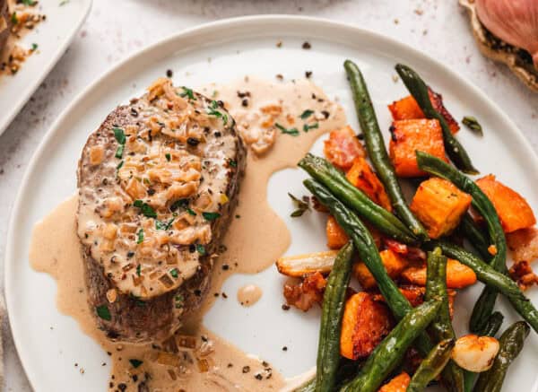 Beef tenderloin steak on a plate with roasted green beans and sweet potatoes