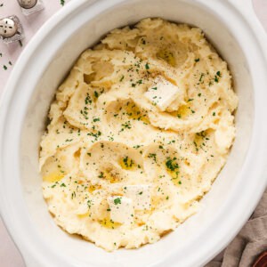 Overhead view of mashed potatoes in a crockpot, topped with pads of butter fresh parsley.