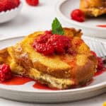 A serving of eggnog French toast casserole on a white plate with berry sauce