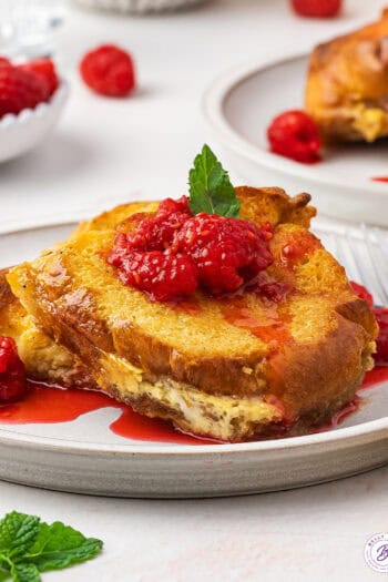 A serving of eggnog French toast casserole on a white plate with berry sauce