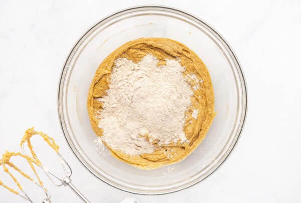 Flour added to the wet ingredients for gingerbread cookies in a glass mixing bowl.