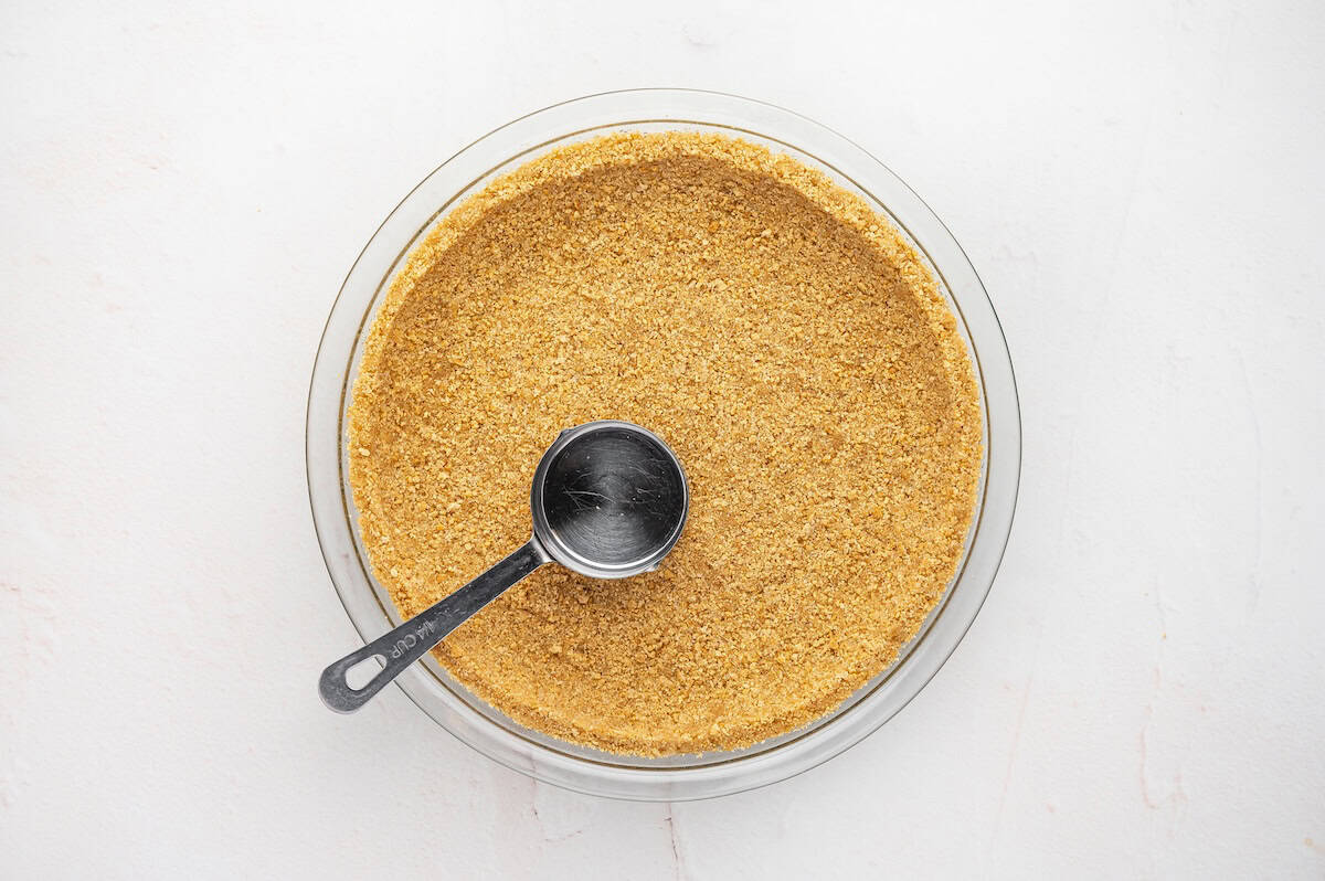 graham cracker crust being pushed down with a spoon in a pie plate