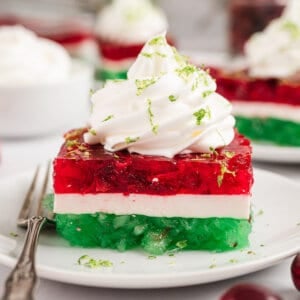 A slice of layered Christmas jello topped with whipped cream on a plate