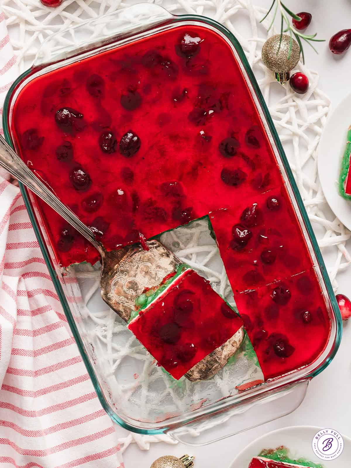 Overhead view of a baking dish of Christmas layered jello with a slice on a serving spatula