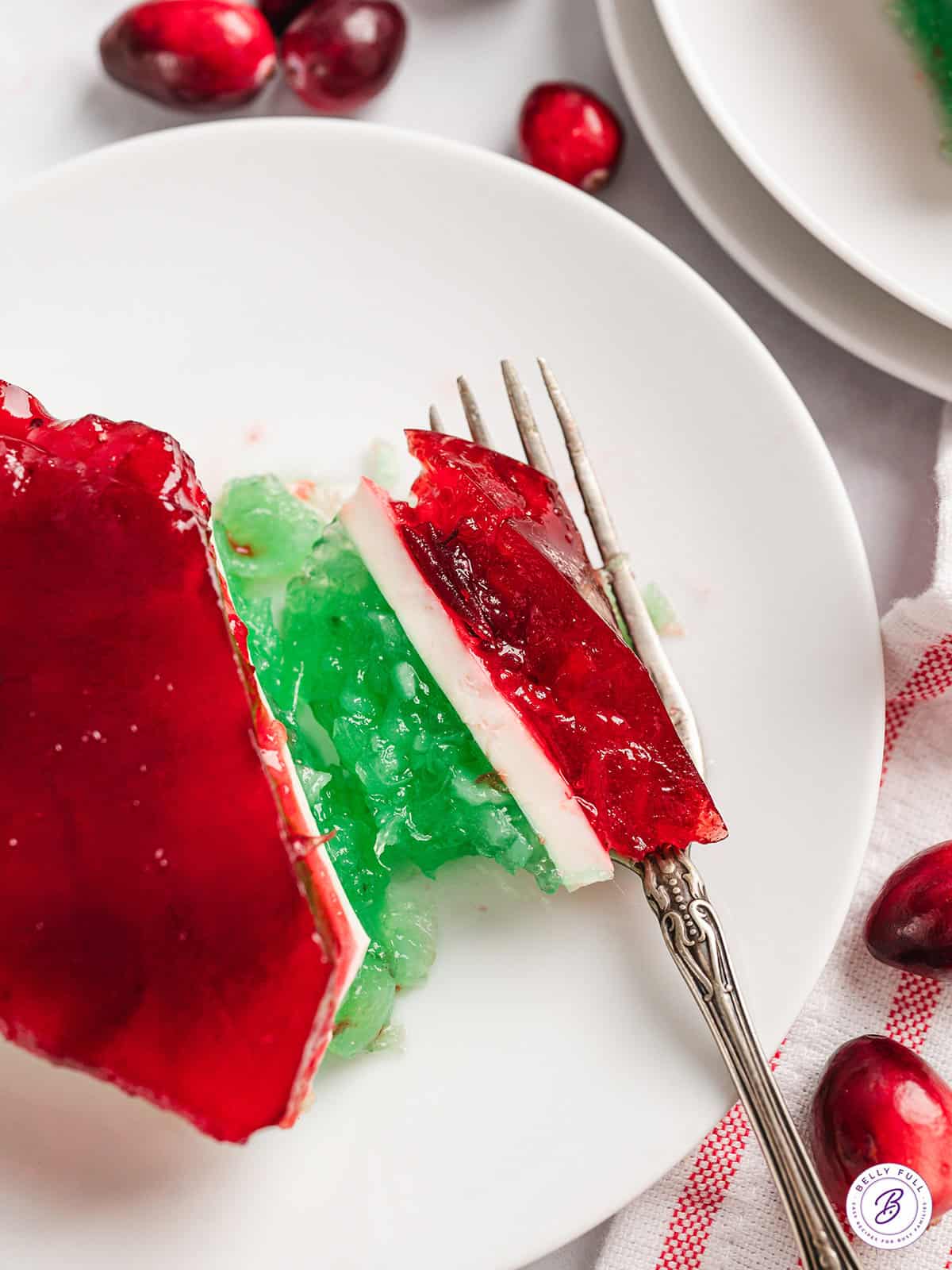 A slice of layered Christmas jello on a white plate with a piece next to a fork