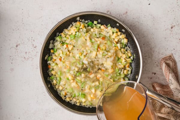 Pouring broth into a skillet with celery, onions, and carrots.