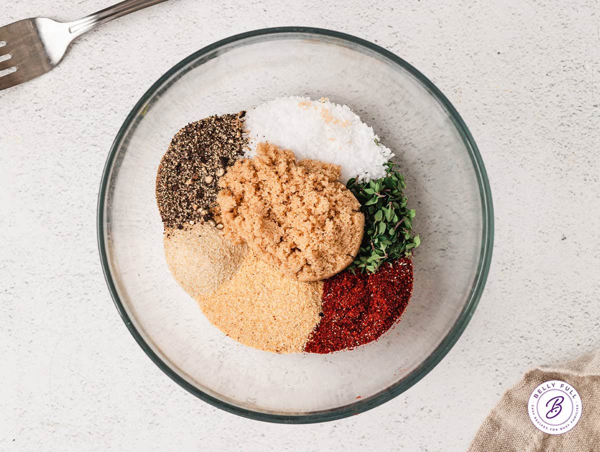 Overhead view of salt, black pepper, rosemary, thyme, onion powder, paprika and brown sugar in a glass mixing bowl.