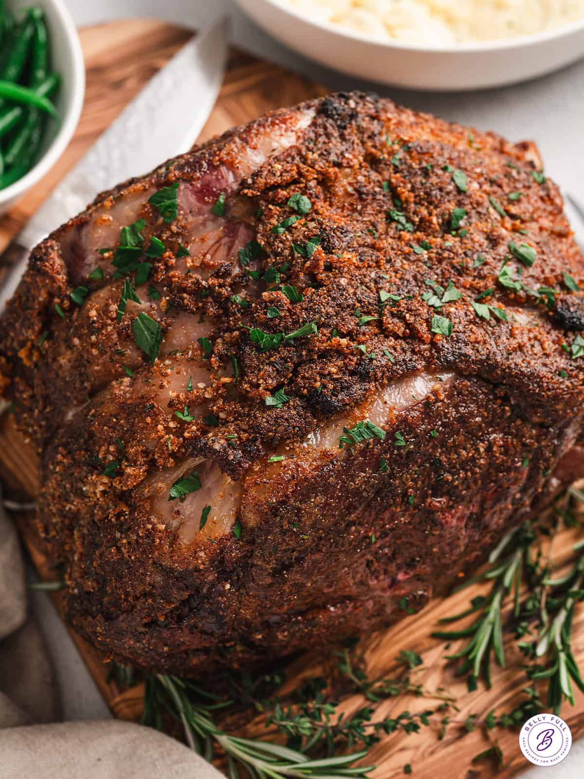 Overhead view of a roasted prime rib, sprinkled with fresh herbs.