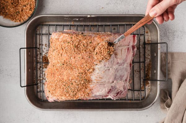 Prime rib rub being sprinkled over a prime rib on a roasting tray.