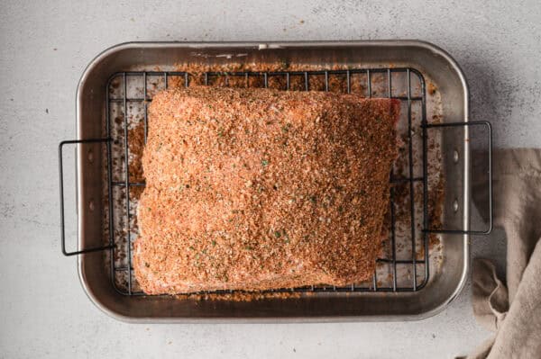 A prime rib roast covered in seasoning rub on a roasting tray.