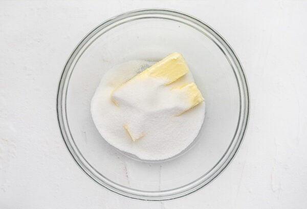 Granulated sugar and two sticks of butter in a glass mixing bowl.