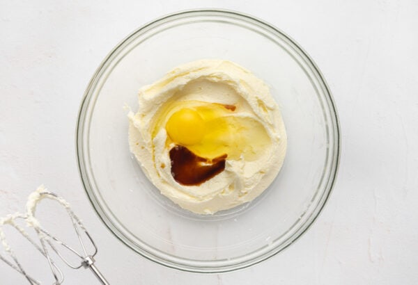 Vanilla extract and eggs added to creamed butter and sugar mixture in a glass mixing bowl.