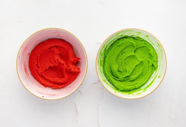 Spritz cookie dough in two bowls, one colored with red food coloring and the other colored with green food coloring.