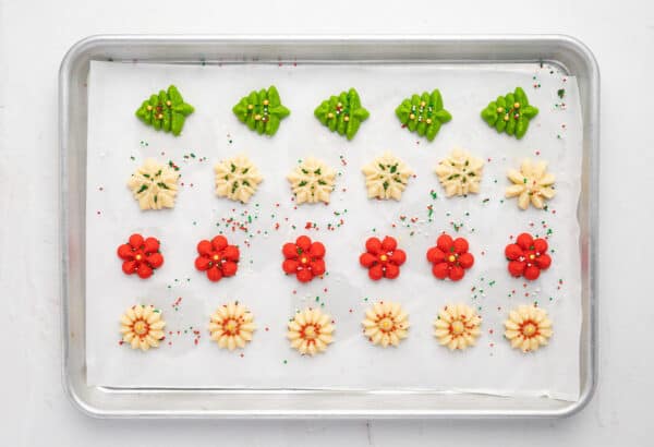 Pressed spritz cookie dough on a parchment lined baking sheet with sprinkles added.