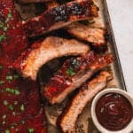 Overhead view of baked baby back ribs on a baking sheet with a side of BBQ sauce