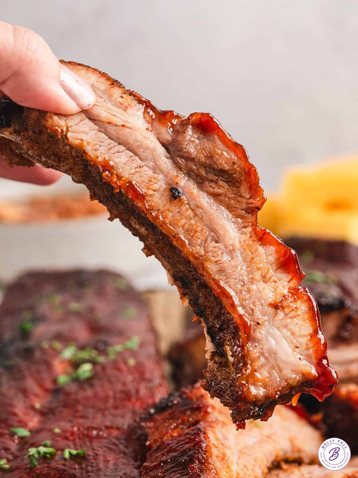 A hand holding a baked baby back rib