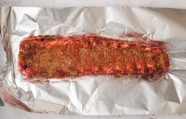 A rack of ribs coated with a spice rub on a piece of foil