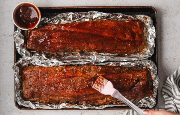 Brushing BBQ sauce on baked racks of ribs on foil