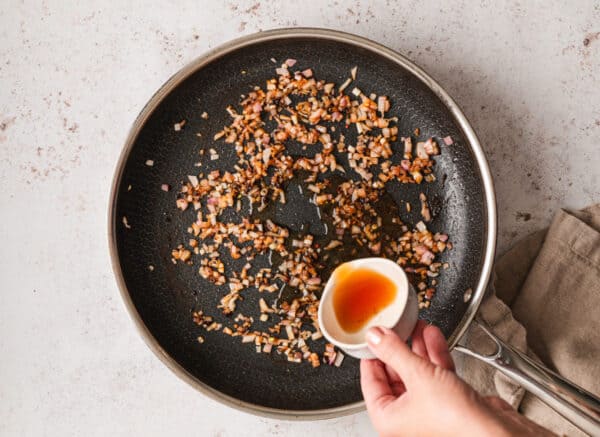 brandy being poured into skillet over sauteed diced shallots