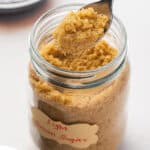 A spoon of brown sugar above a jar of brown sugar