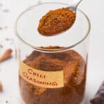 A glass jar of chili seasoning with a spoon of seasoning over the jar