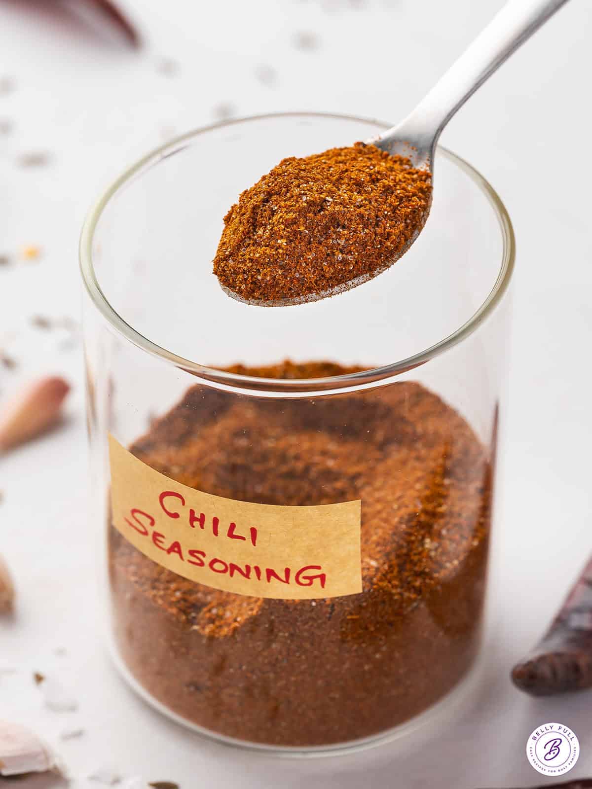 A glass jar of chili seasoning with a spoon of seasoning over the jar