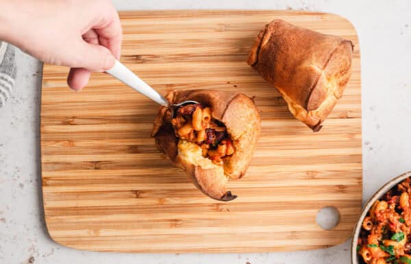 A spoon adding chili mac to a popover